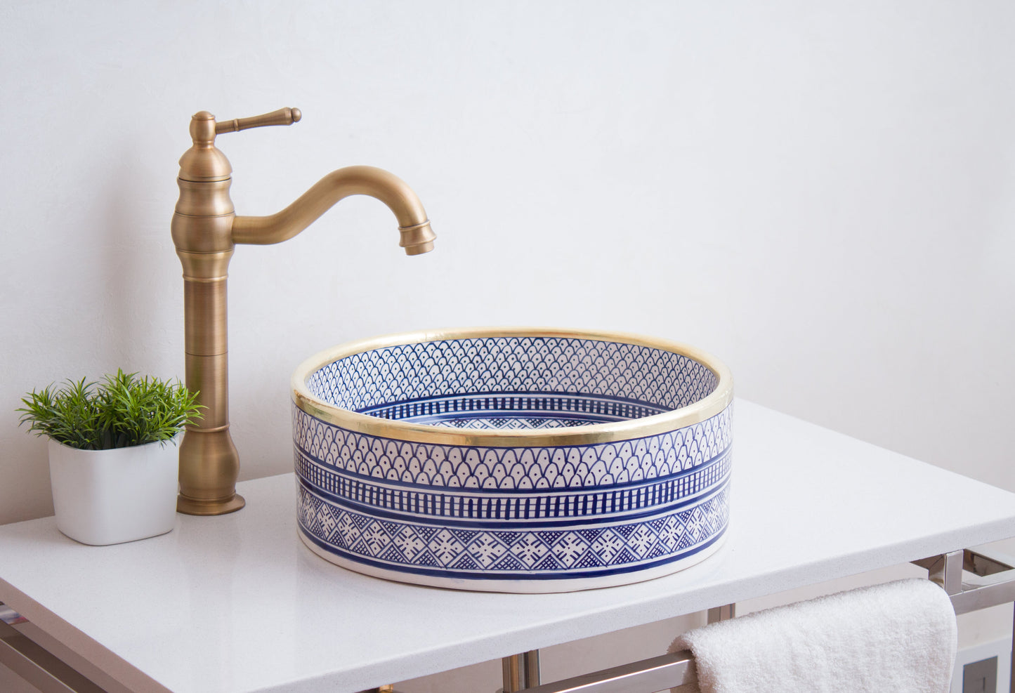 Round Moroccan ceramic basin installed on white bathroom vanity with traditional brass faucet and decorative plant