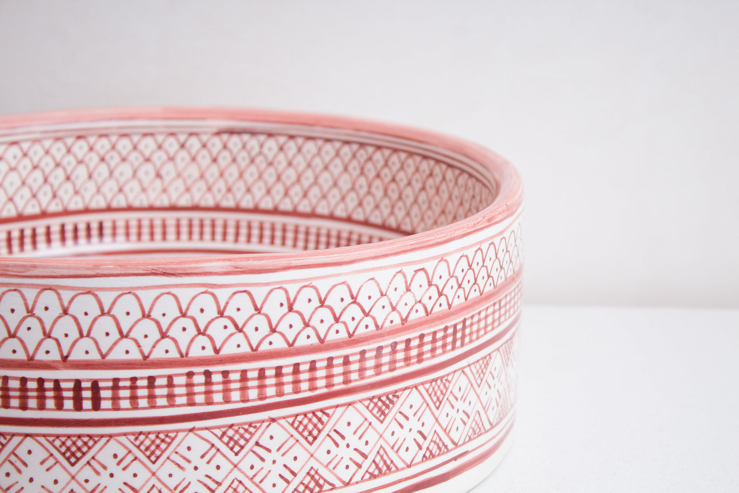 Macro close-up detail of intricate coral pink and white geometric pattern bands around the exterior rim of handcrafted ceramic basin