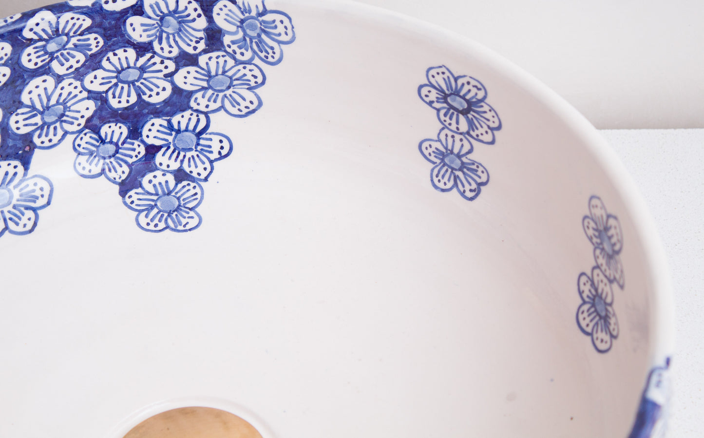 Close-up interior detail of ceramic vessel sink showing blue flower clusters and scattered blooms with drain opening and smooth finish