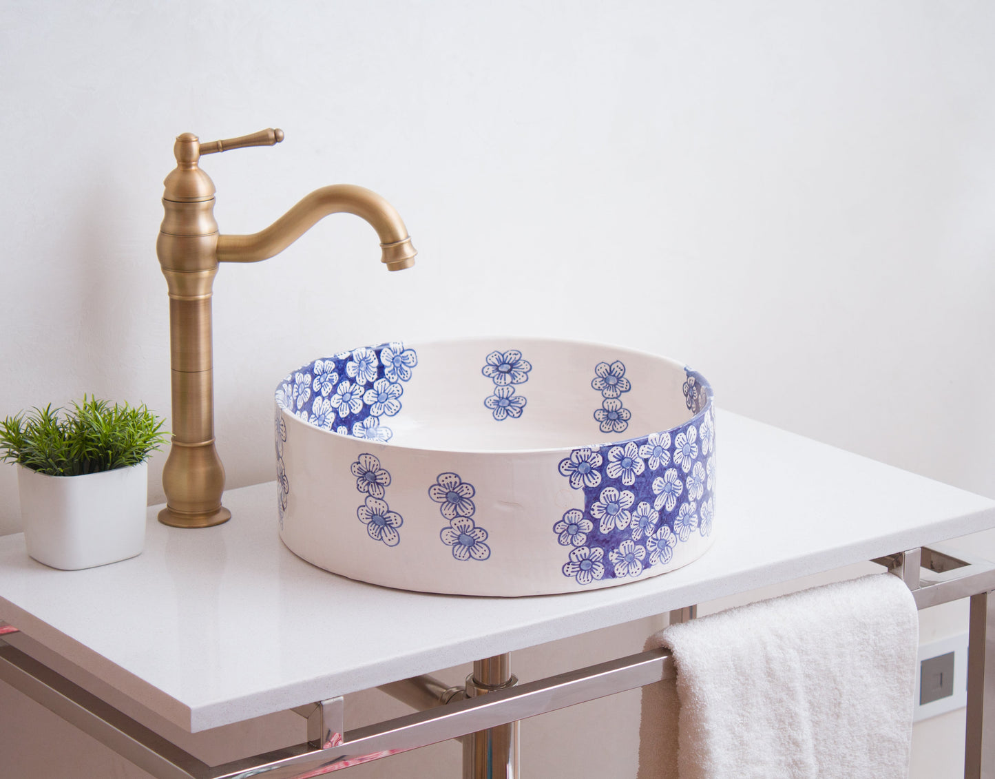 Blue floral ceramic vessel sink on white contemporary vanity with brass traditional faucet and decorative green plant in modern bathroom