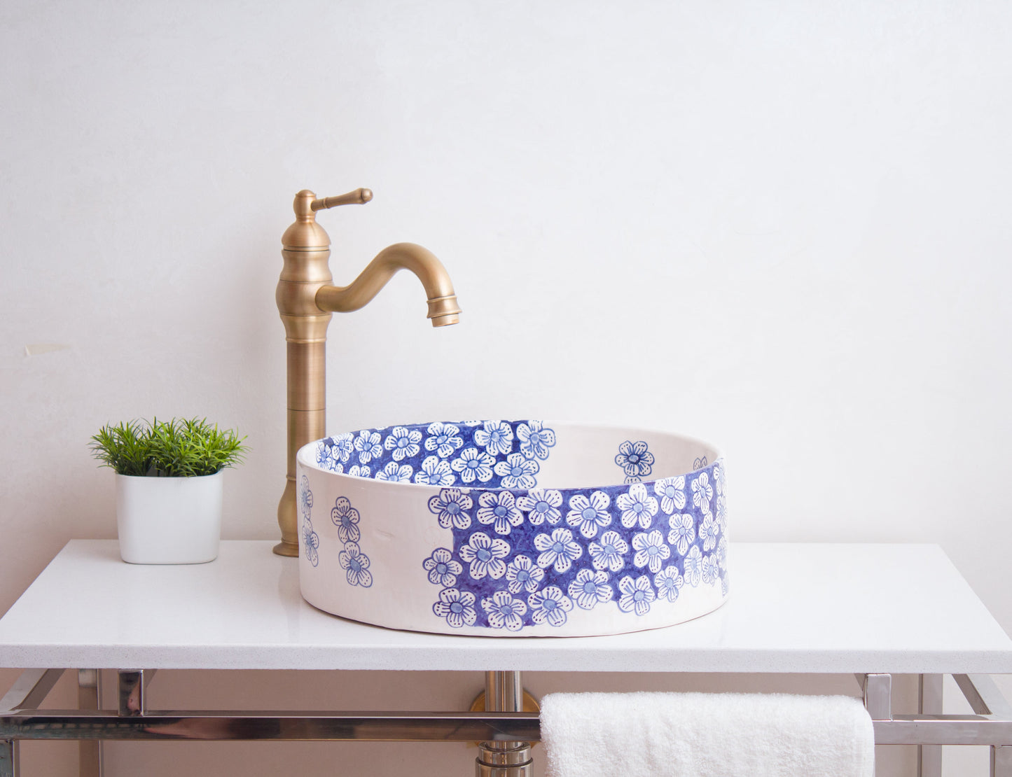 Ceramic vessel sink with blue flower clusters on white floating vanity with tall brass faucet and white towel in contemporary bathroom setting