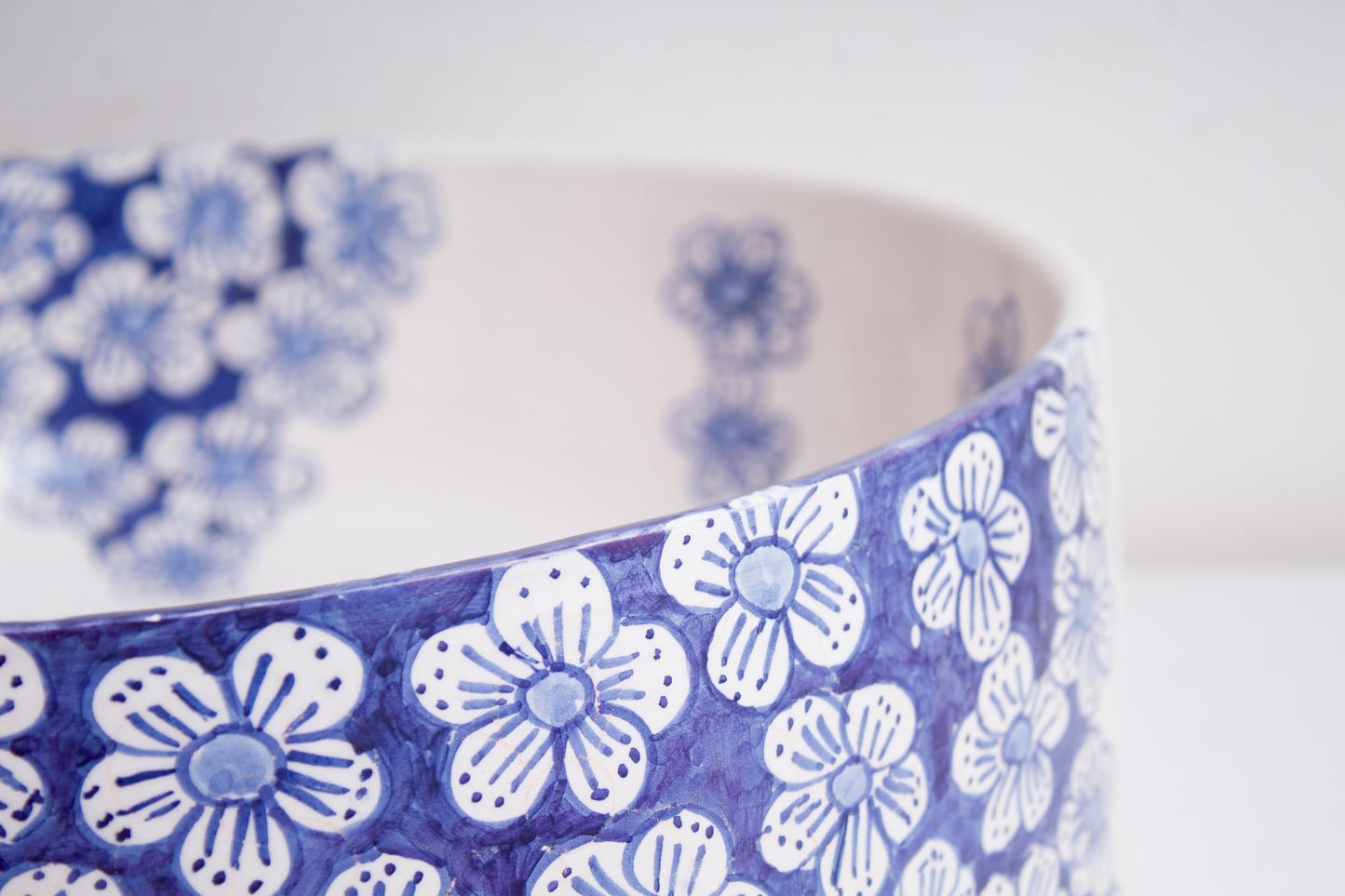 Close-up detail of ceramic vessel sink rim highlighting the hand-painted blue floral pattern and delicate flower motifs