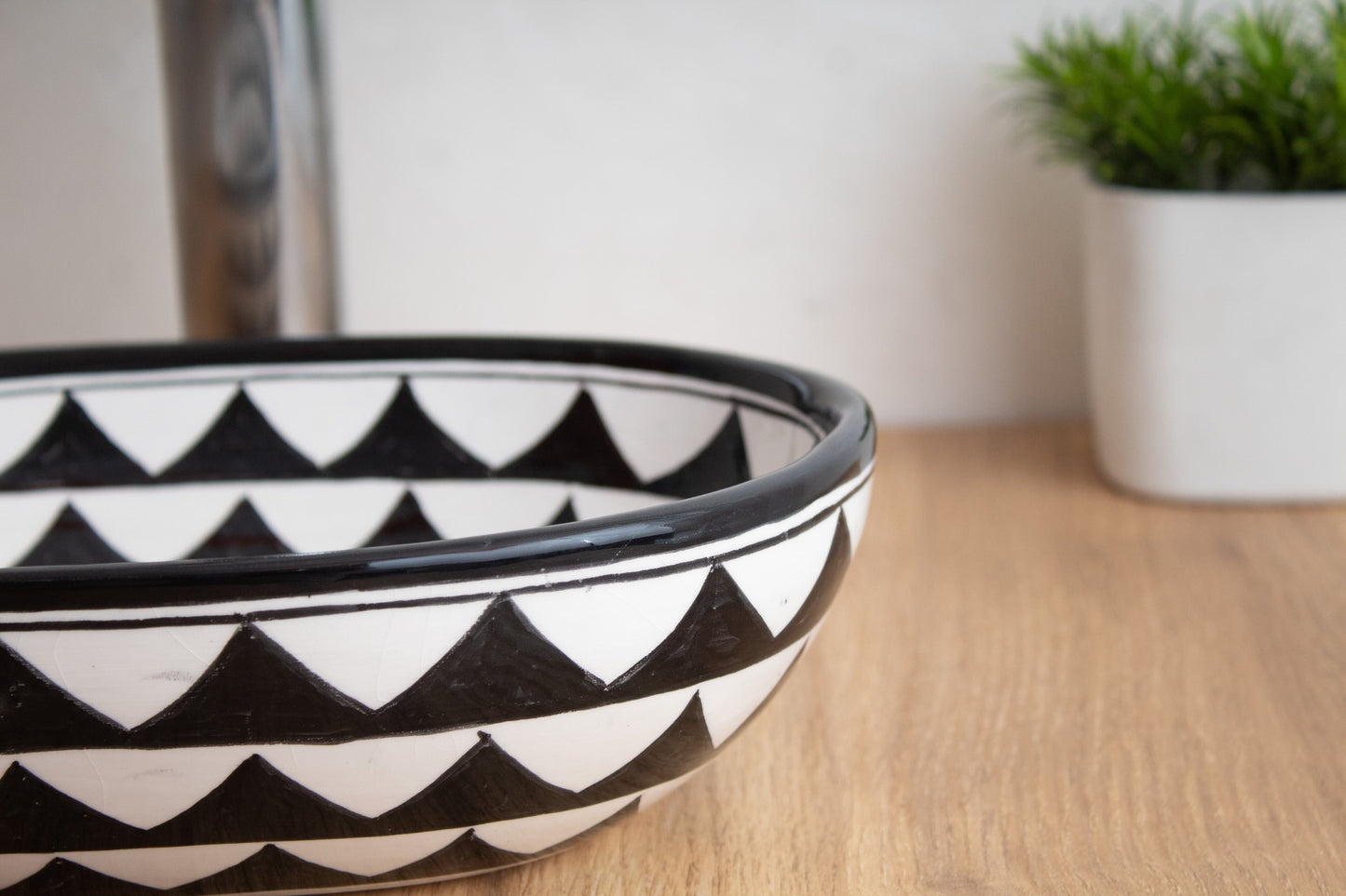 Close-up edge detail of tiny oval ceramic vessel sink showing the triangular pattern and glossy finish on contemporary wood surface