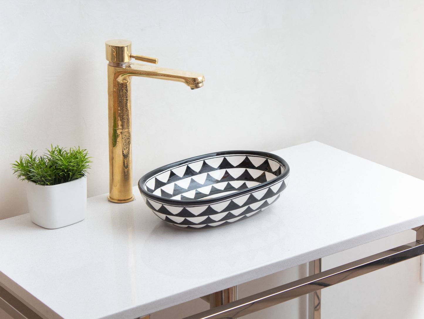 Small oval ceramic vessel sink with triangle pattern on white contemporary vanity with tall brass faucet and decorative green plant