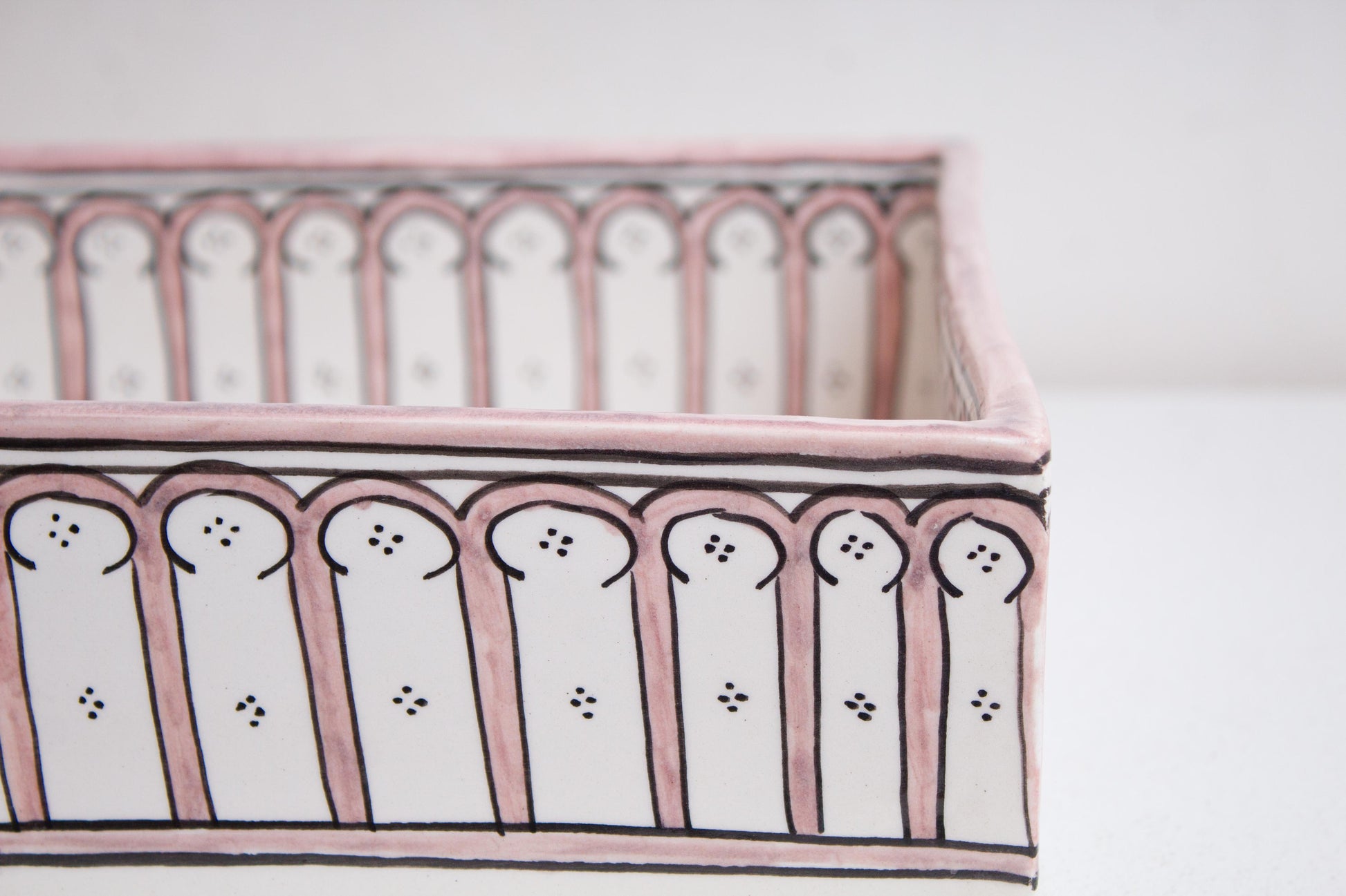 Close-up detail of handpainted pink arch colonnade pattern on exterior walls of artisan-crafted Moroccan ceramic bathroom basin