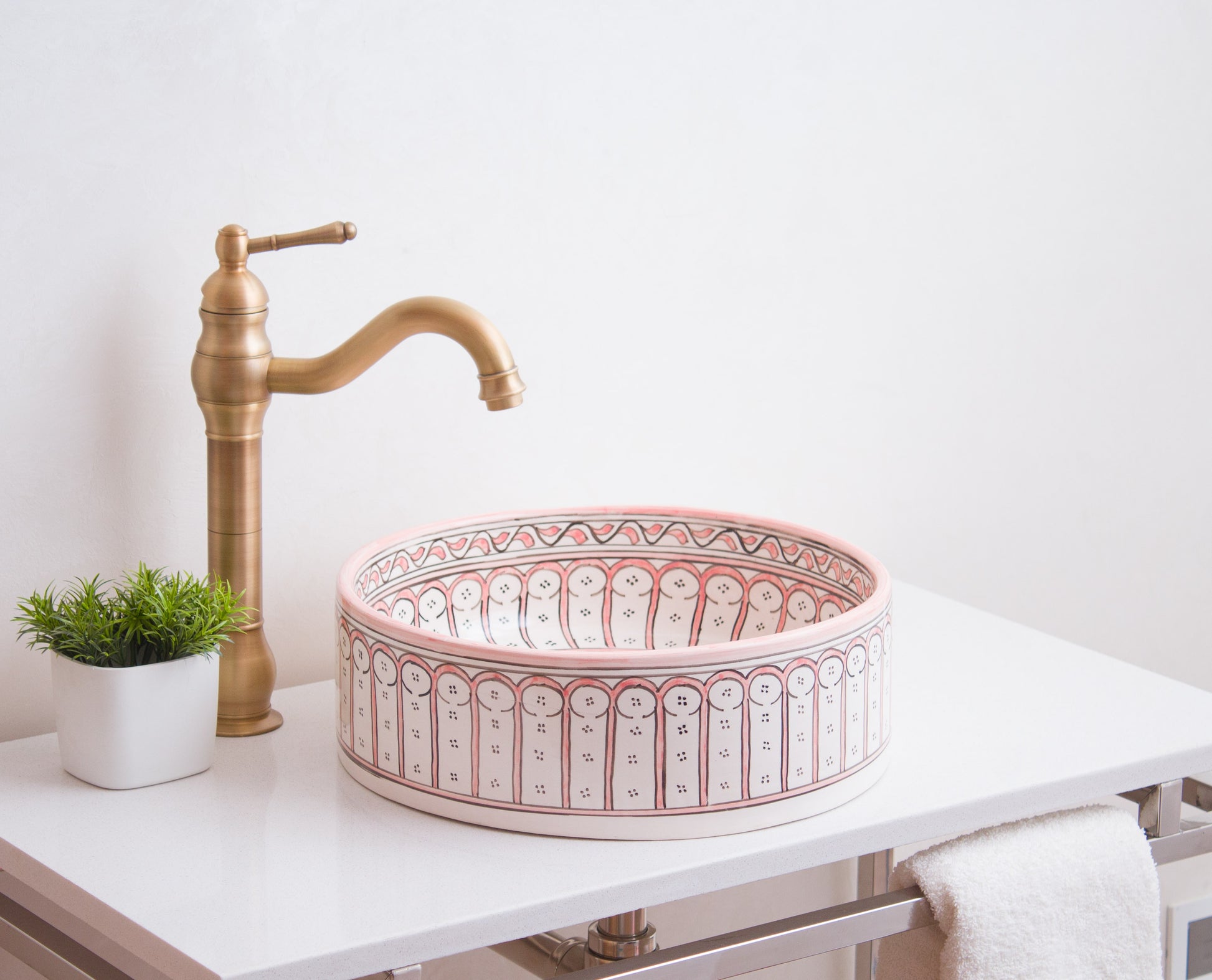 Round Moroccan ceramic basin installed on white bathroom vanity with traditional brass faucet and decorative plant