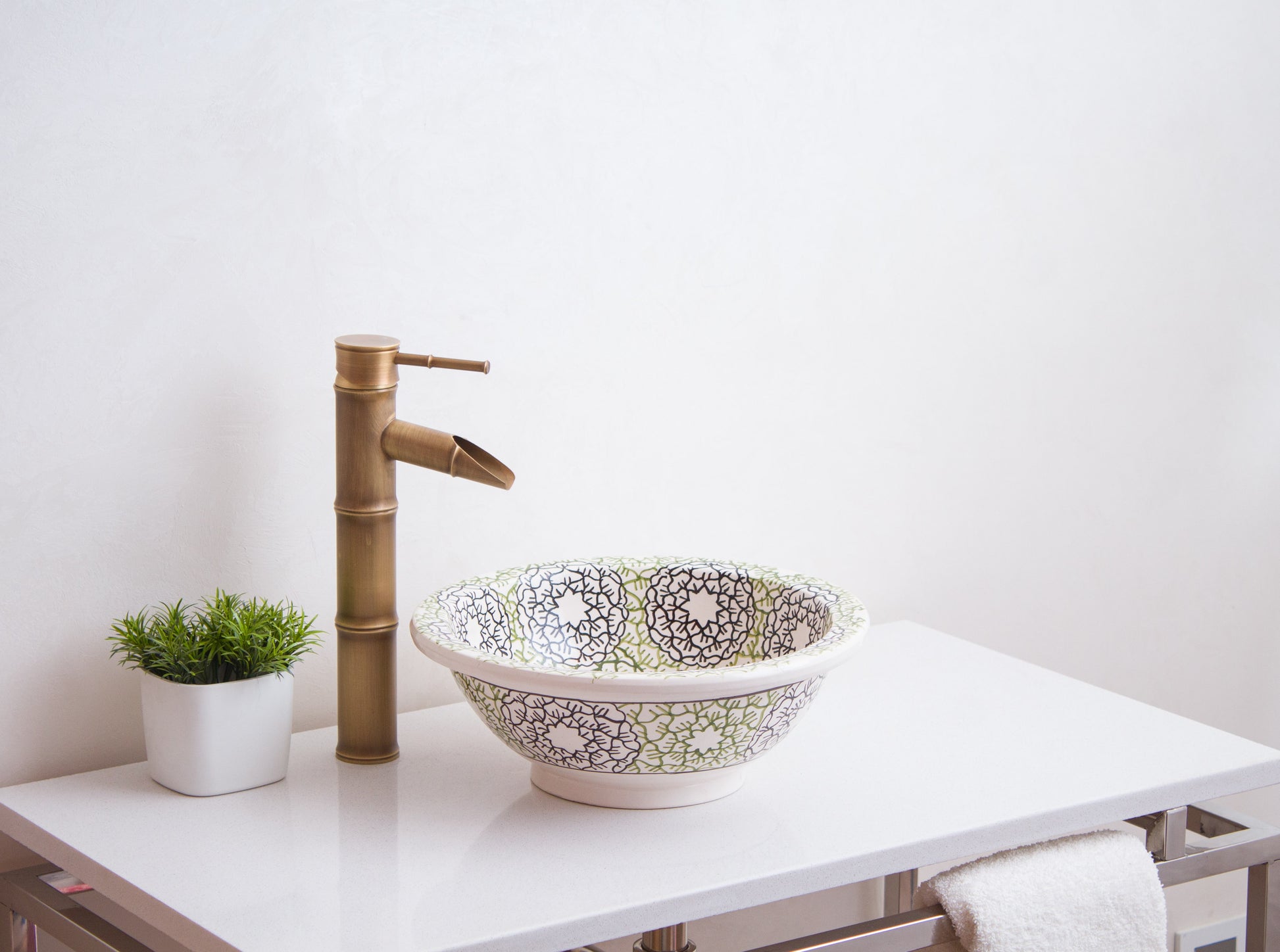 Moroccan ceramic wash basin styled on white vanity with brass bamboo faucet and decorative plant