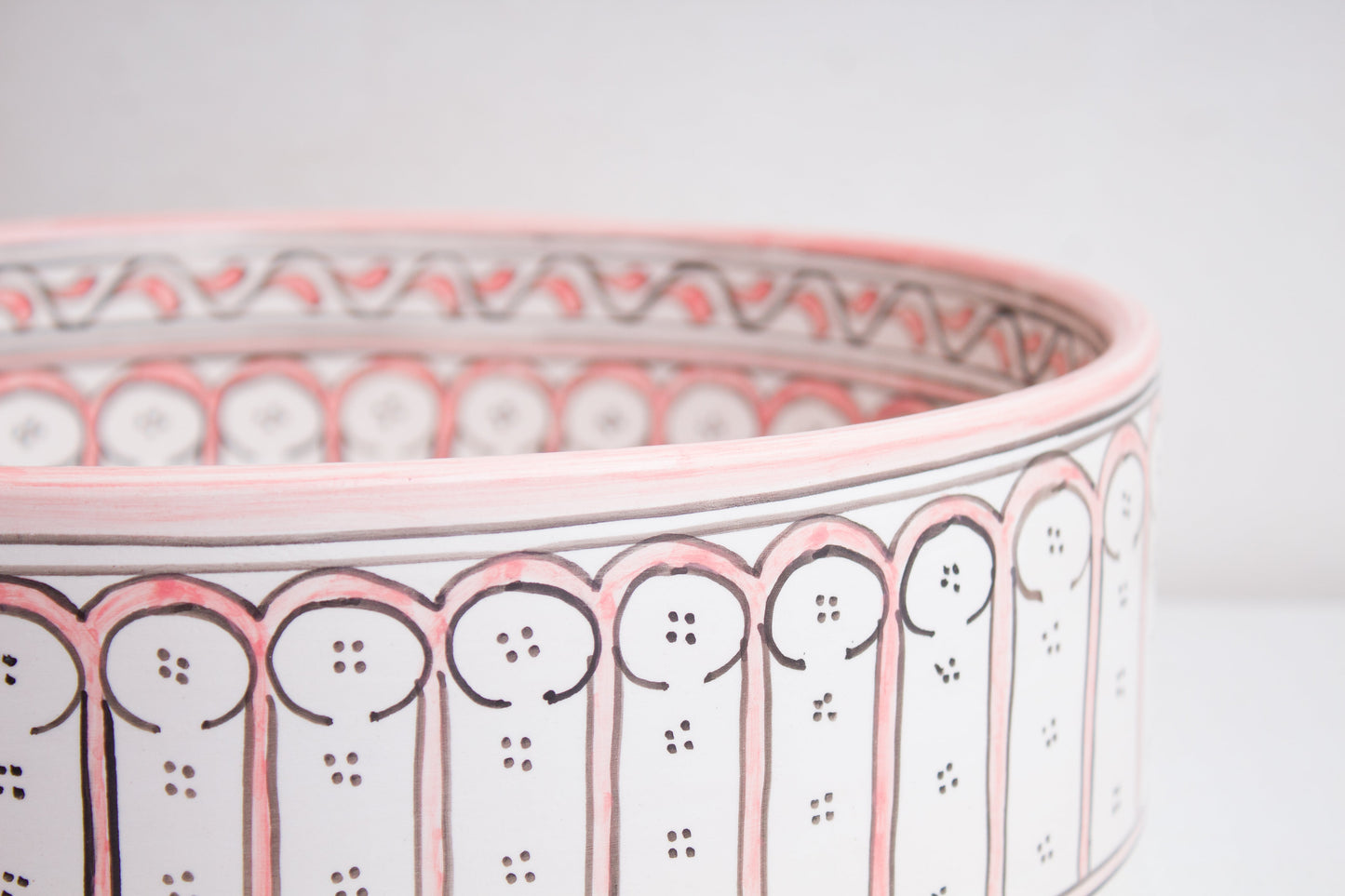 Macro close-up detail of intricate coral pink and white Moorish arch pattern around the exterior rim of handcrafted ceramic basin