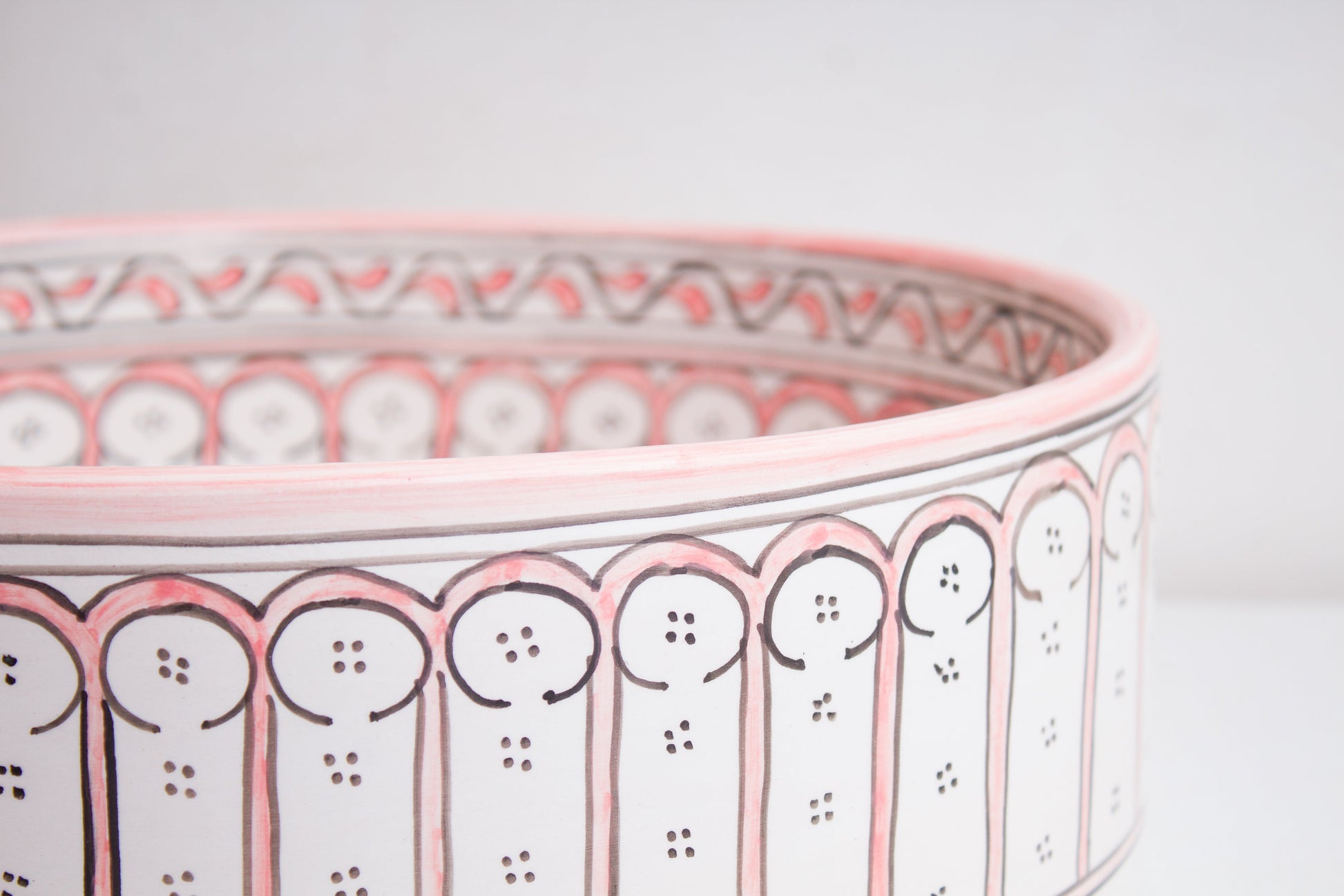 Macro close-up detail of intricate coral pink and white Moorish arch pattern around the exterior rim of handcrafted ceramic basin