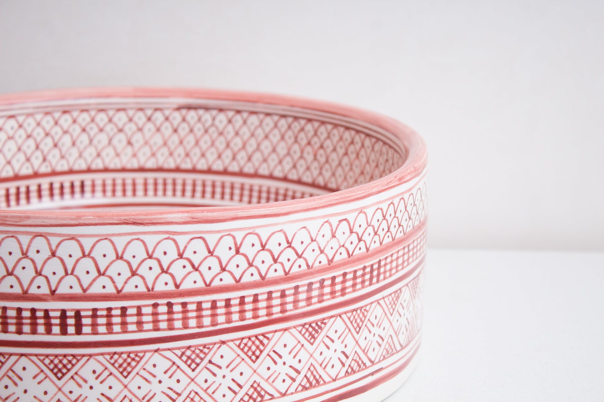 Macro close-up detail of intricate coral pink and white geometric pattern bands around the exterior rim of handcrafted ceramic basin