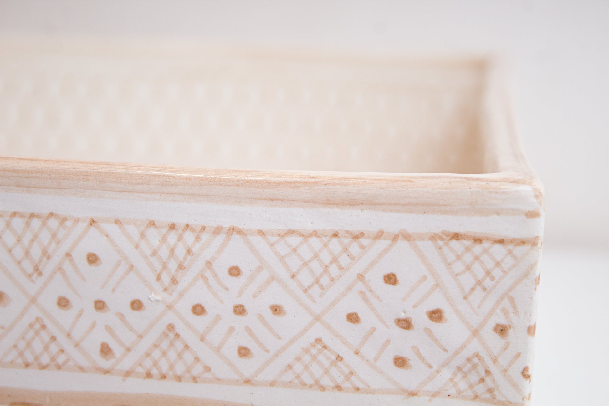 Close-up detail of intricate diamond and dot patterns on beige ceramic basin exterior rim