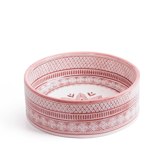 Three-quarter perspective view of handcrafted round ceramic basin featuring coral pink and white geometric patterns