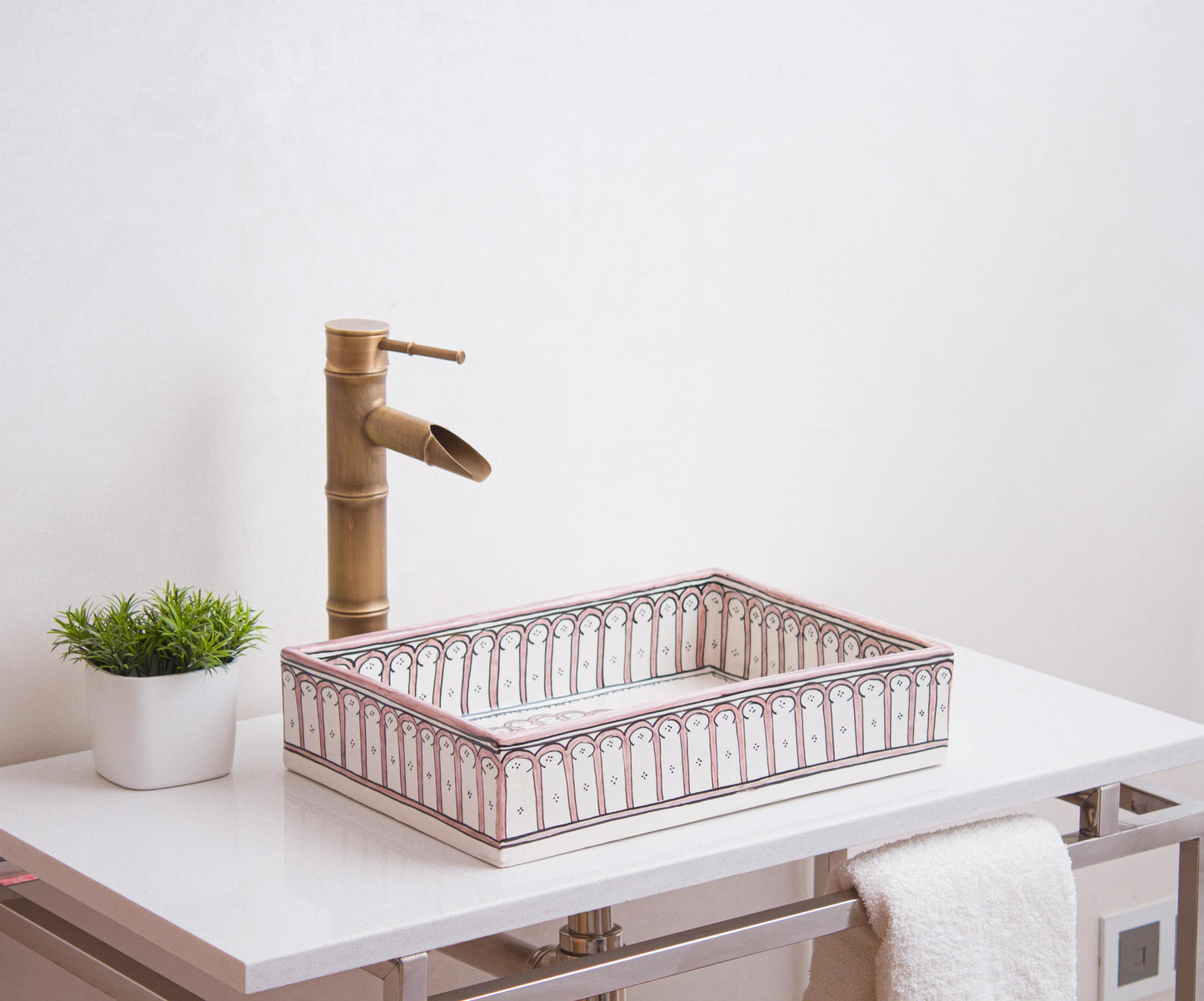 Handcrafted Moroccan ceramic rectangular sink with pink arch colonnade pattern displayed on white vanity with bamboo faucet and decorative plant