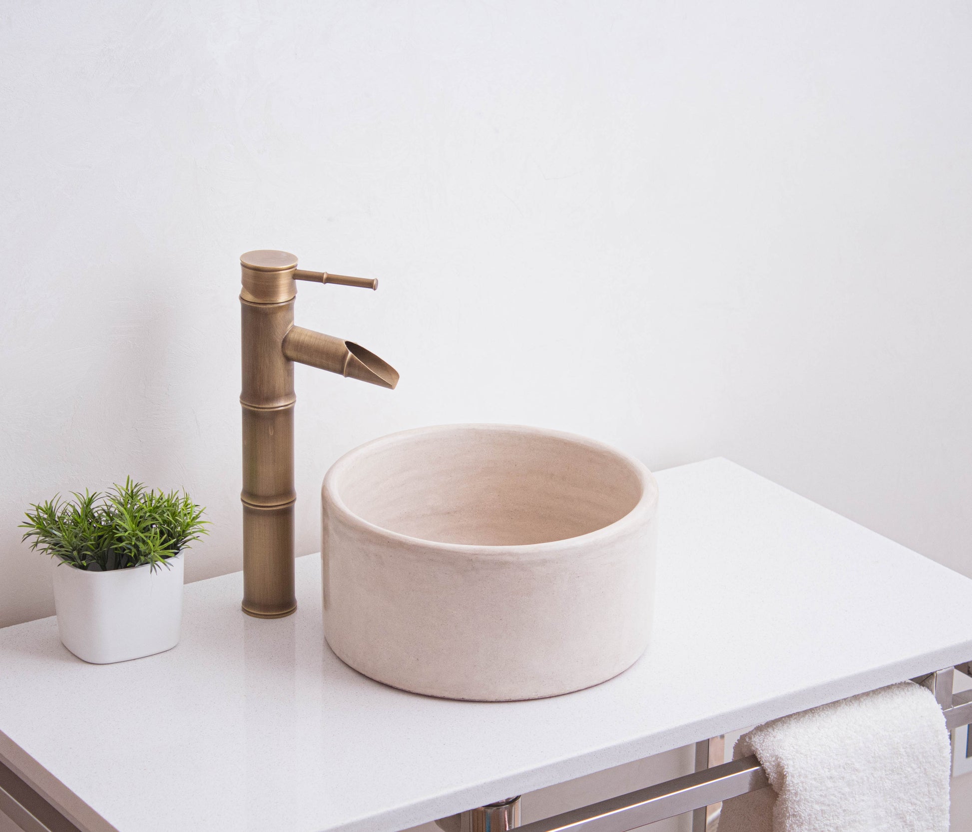Handcrafted Moroccan round ceramic sink in beige tadelakt finish displayed on white vanity with bamboo faucet and decorative plant