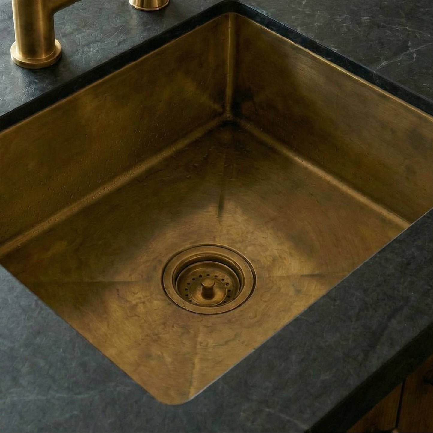 Antique brass kitchen sink with gold faucet on a dark countertop