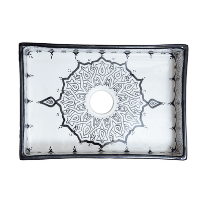 Top-down view of a handmade Moroccan rectangular ceramic bathroom sink, showcasing a central black geometric starburst pattern around the drain and a dark contrasting rim.