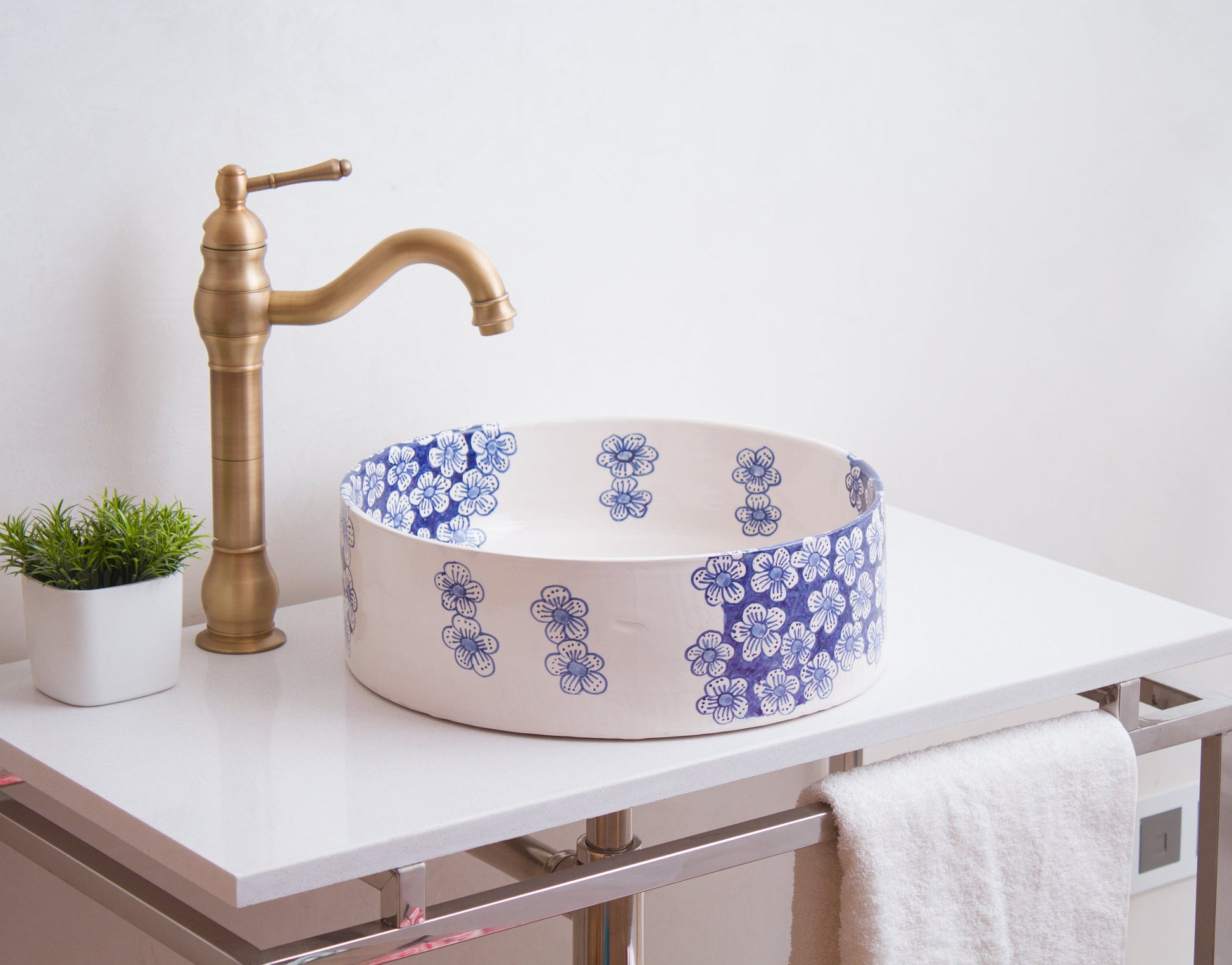 Blue floral ceramic vessel sink on white contemporary vanity with brass traditional faucet and decorative green plant in modern bathroom