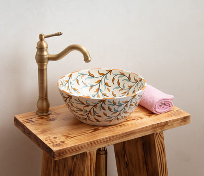 Ceramic vessel sink with hand-painted olive branch design styled on rustic wooden vanity with brass faucet and pink towel