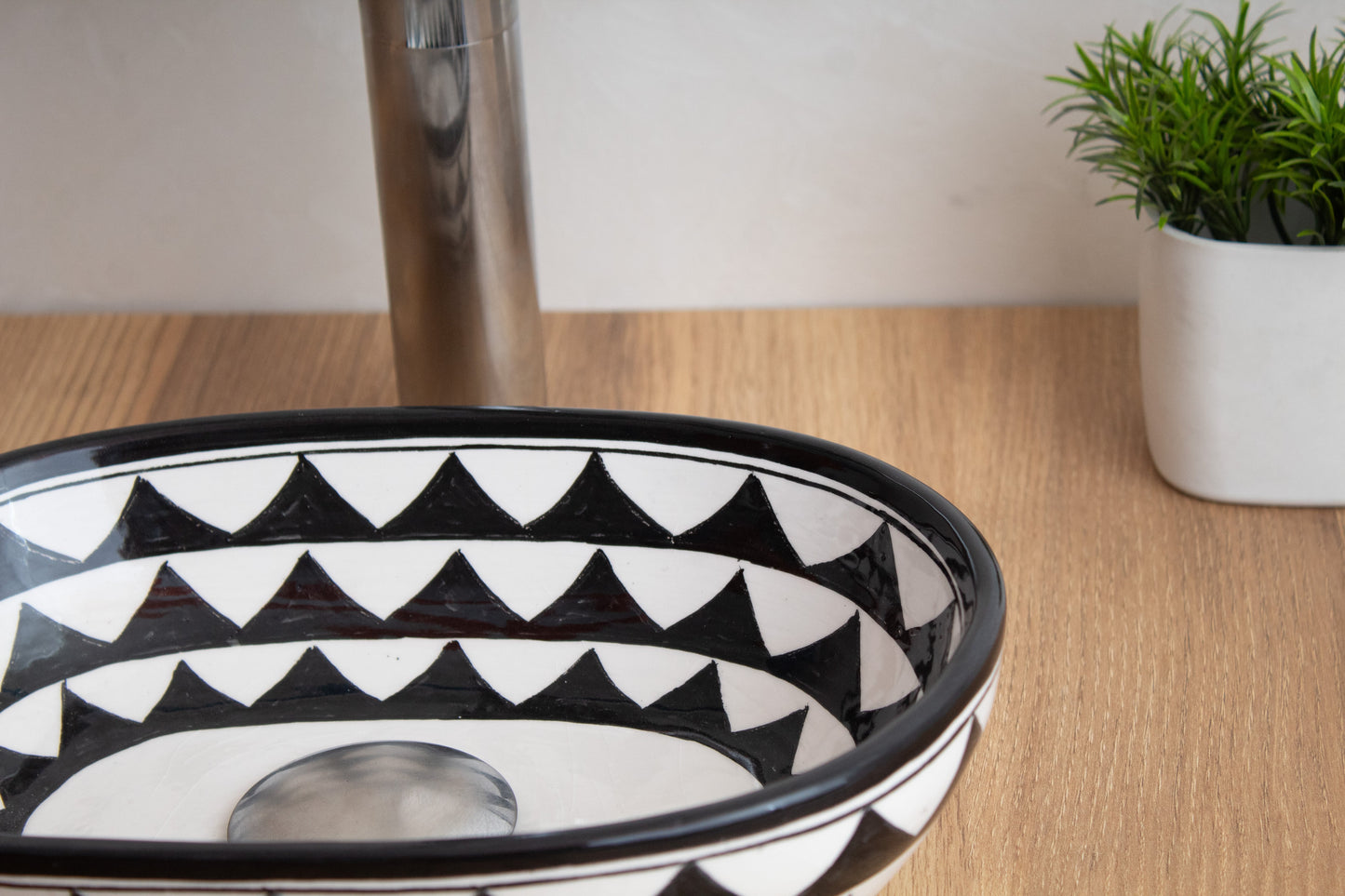 Close-up detail of compact oval ceramic vessel sink rim highlighting the black and white geometric triangle pattern on wood surface