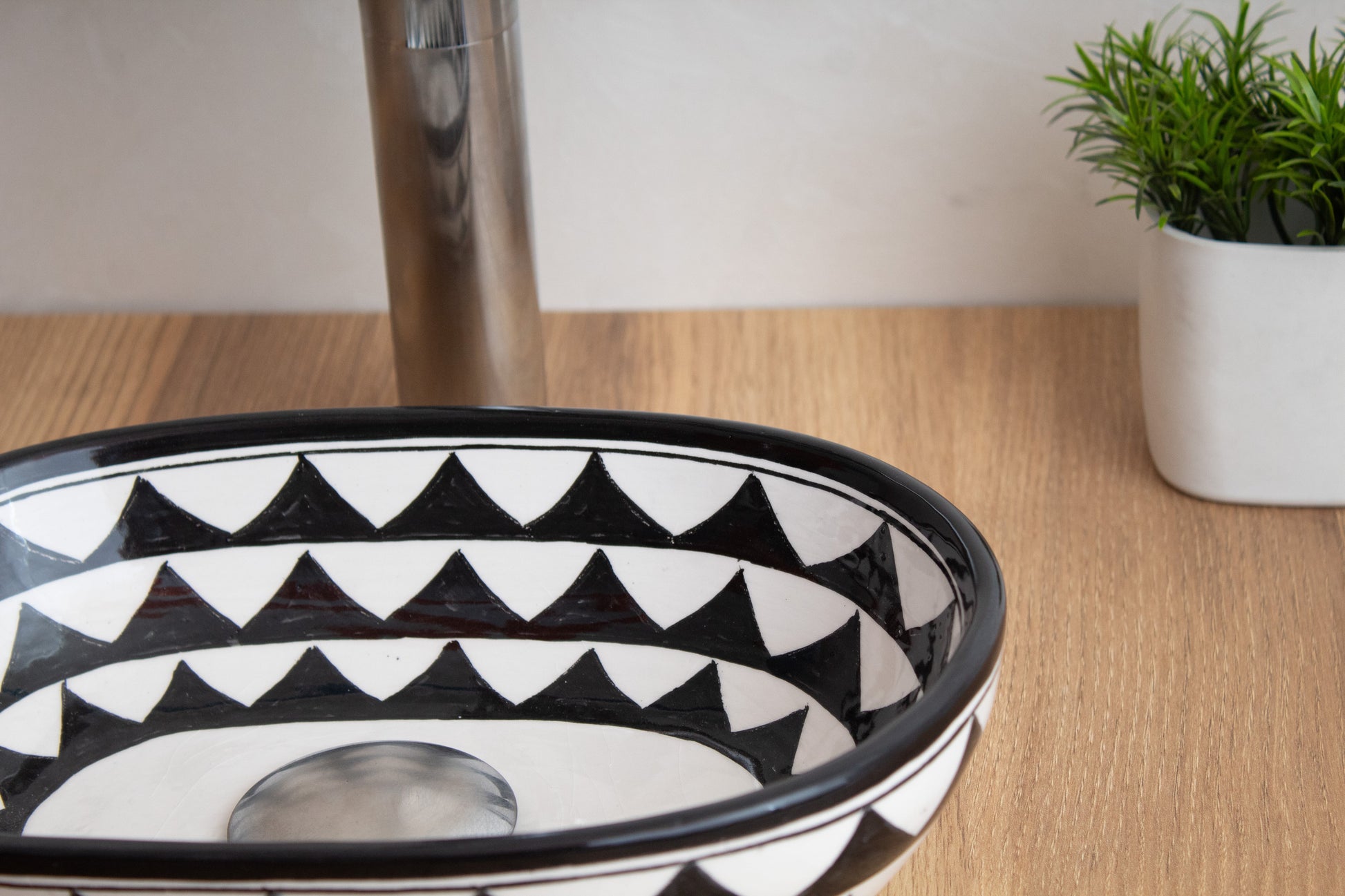 Close-up detail of compact oval ceramic vessel sink rim highlighting the black and white geometric triangle pattern on wood surface