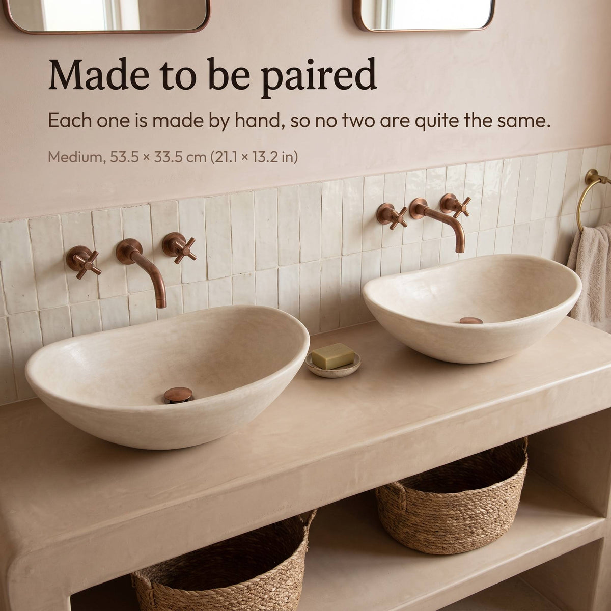 Two medium beige tadelakt vessel sinks, 53.5 x 33.5 cm (21.1 x 13.2 in), side by side on a plaster vanity with copper wall faucets and white zellige tiles