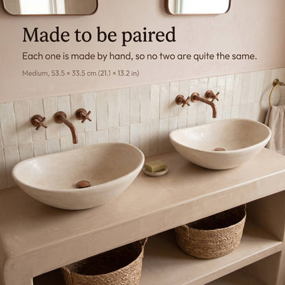 Two medium beige tadelakt vessel sinks, 53.5 x 33.5 cm (21.1 x 13.2 in), side by side on a plaster vanity with copper wall faucets and white zellige tiles