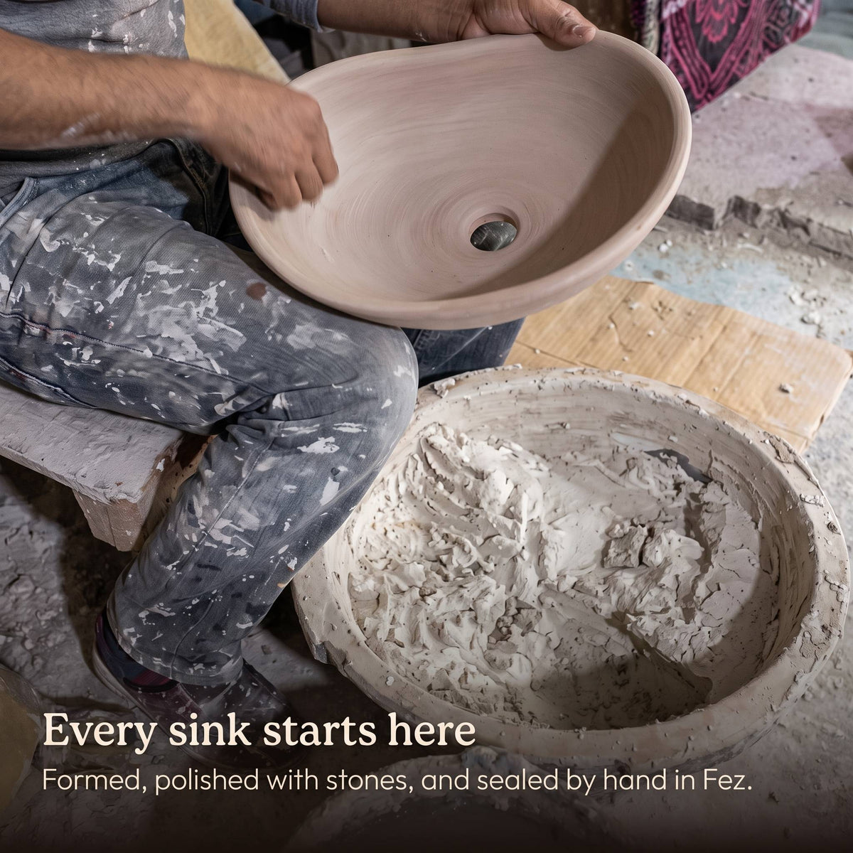 Skilled artisan in a Fez workshop shaping an unfinished oval sink by hand, beside a tub of lime plaster, before it is stone-polished and sealed