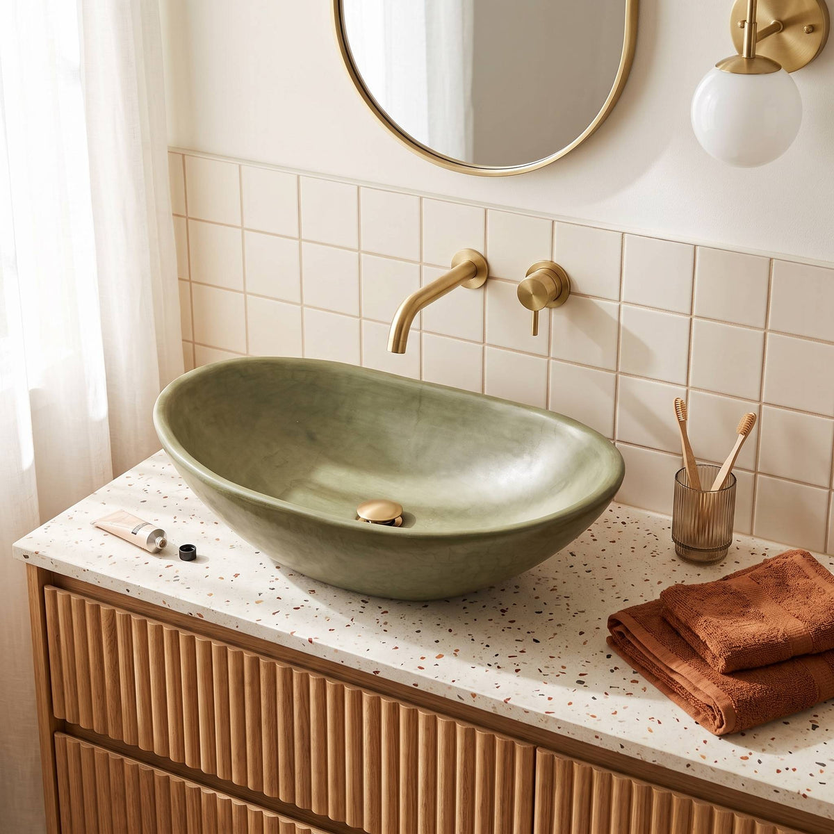 An olive green Tadelakt medium size vessel sink basin, set on a speckled white countertop with a ribbed wood vanity.