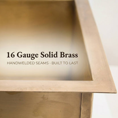 Close-up of the corner and rim of a handmade rectangular aged brass undermount kitchen sink, highlighting the 16 gauge solid brass thickness, flat mounting rim, and hand-welded seams.
