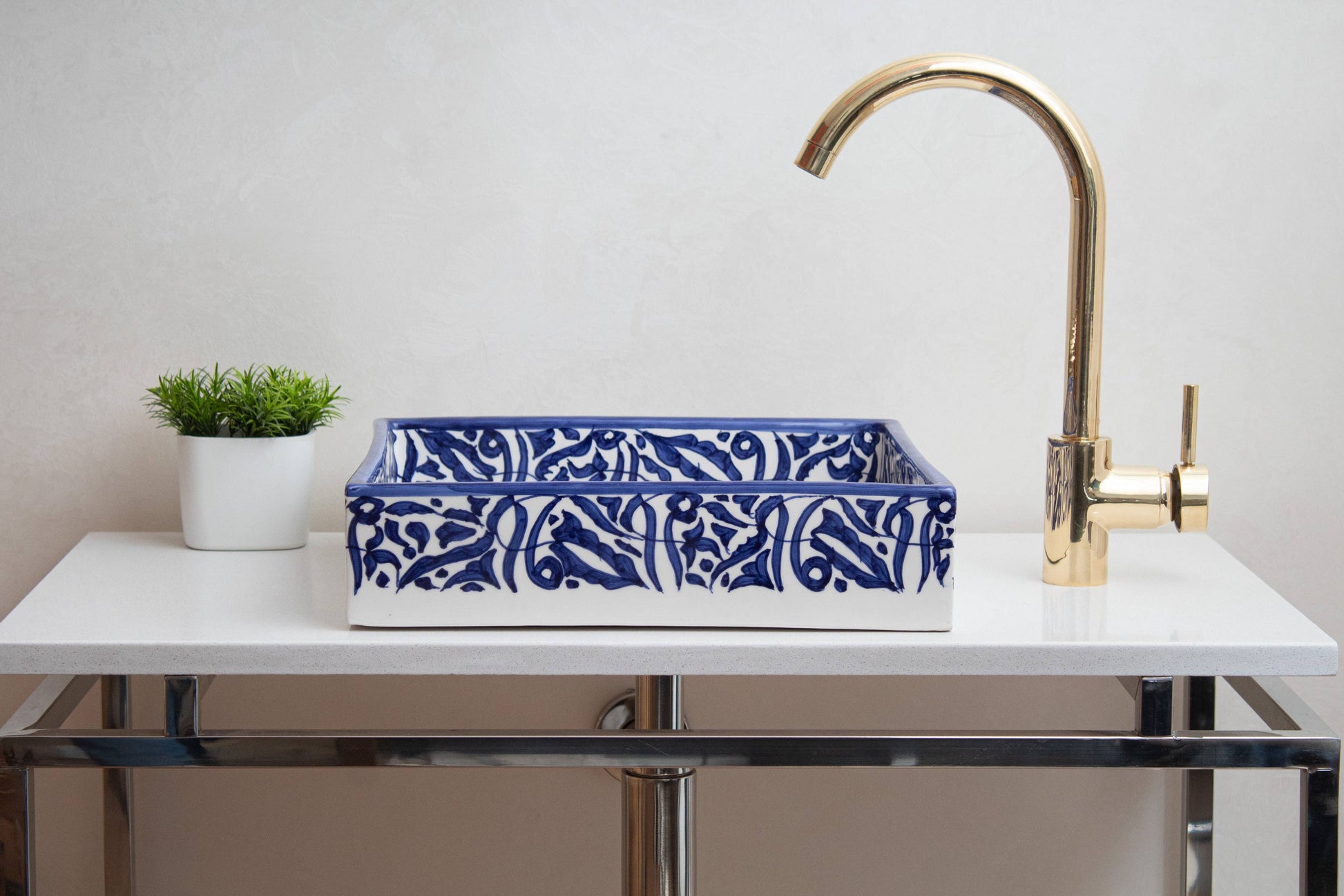 Navy blue and white ceramic vessel sink on white vanity with brass gooseneck faucet and green plant