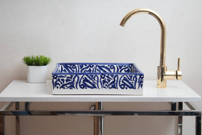 Navy blue and white ceramic vessel sink on white vanity with brass gooseneck faucet and green plant
