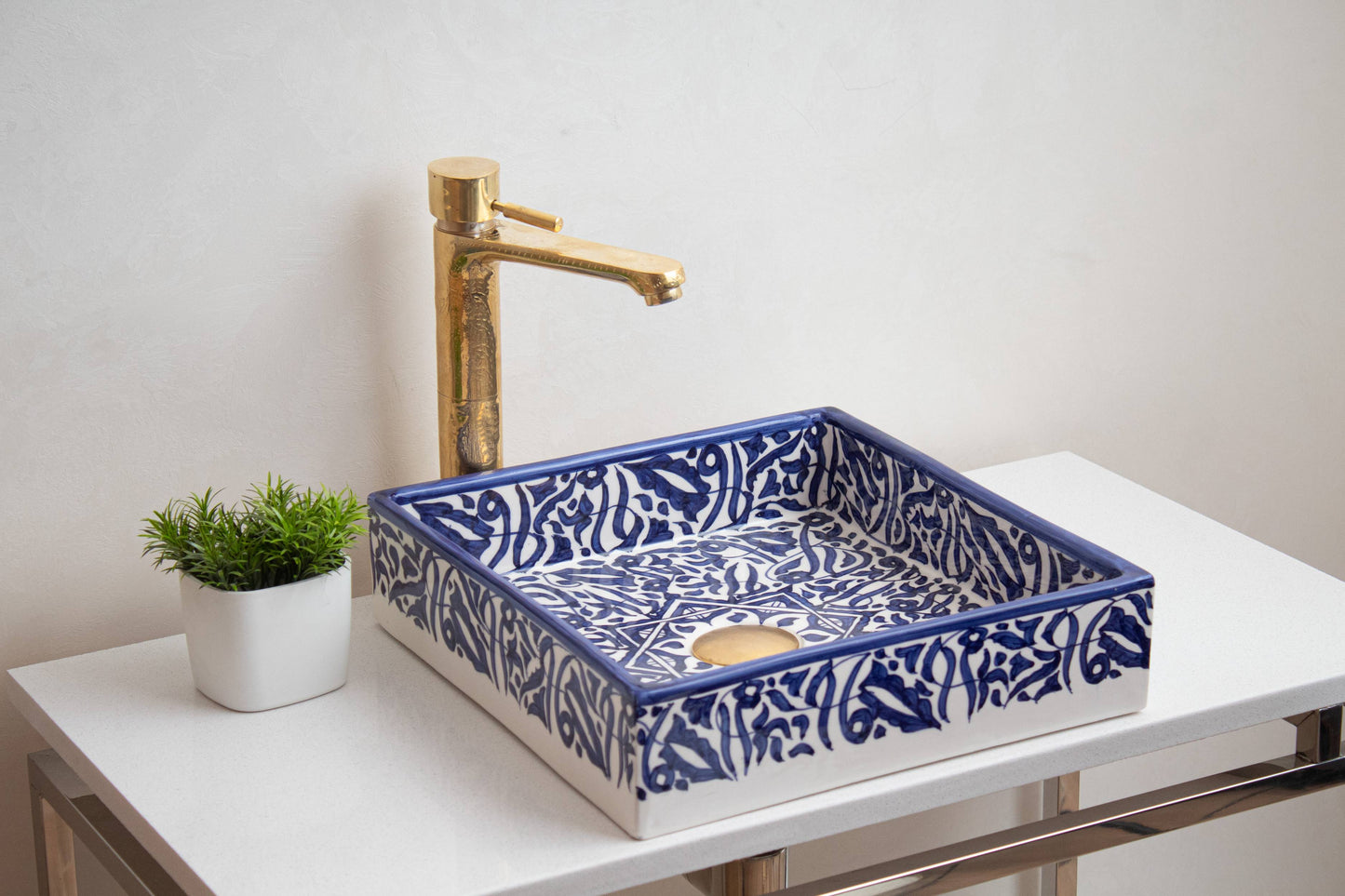 Blue Moroccan ceramic bathroom sink with brass faucet on white countertop beside decorative plant