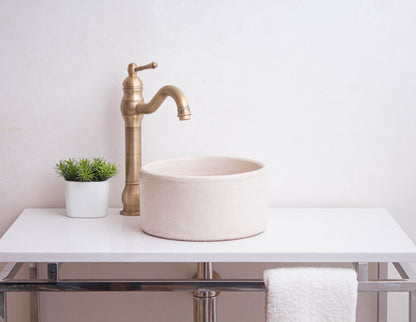 Round ceramic vessel sink with tadelakt finish positioned on modern bathroom vanity with vintage brass faucet and decorative accessories