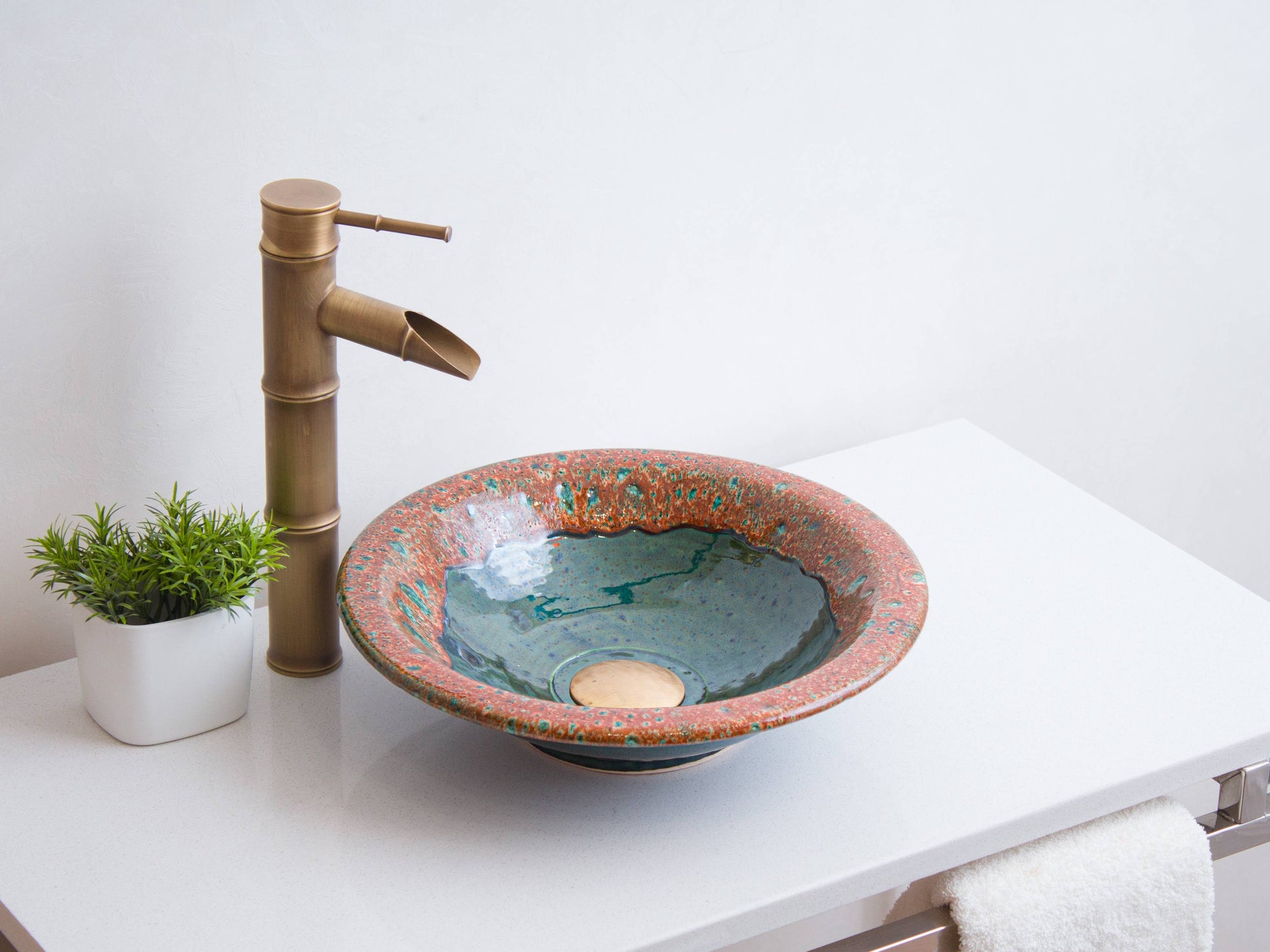Coral and teal ceramic bathroom sink on white vanity with brass bamboo-style faucet