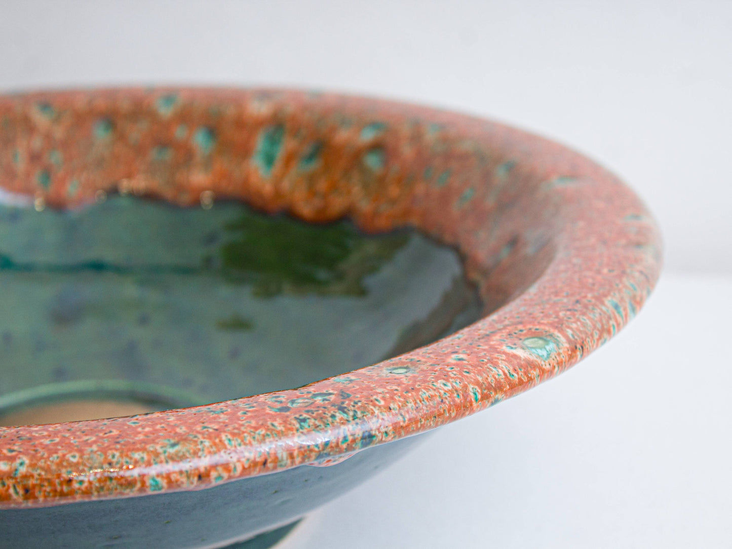 Close-up of hand-painted turquoise speckles on coral glazed rim of ceramic sink