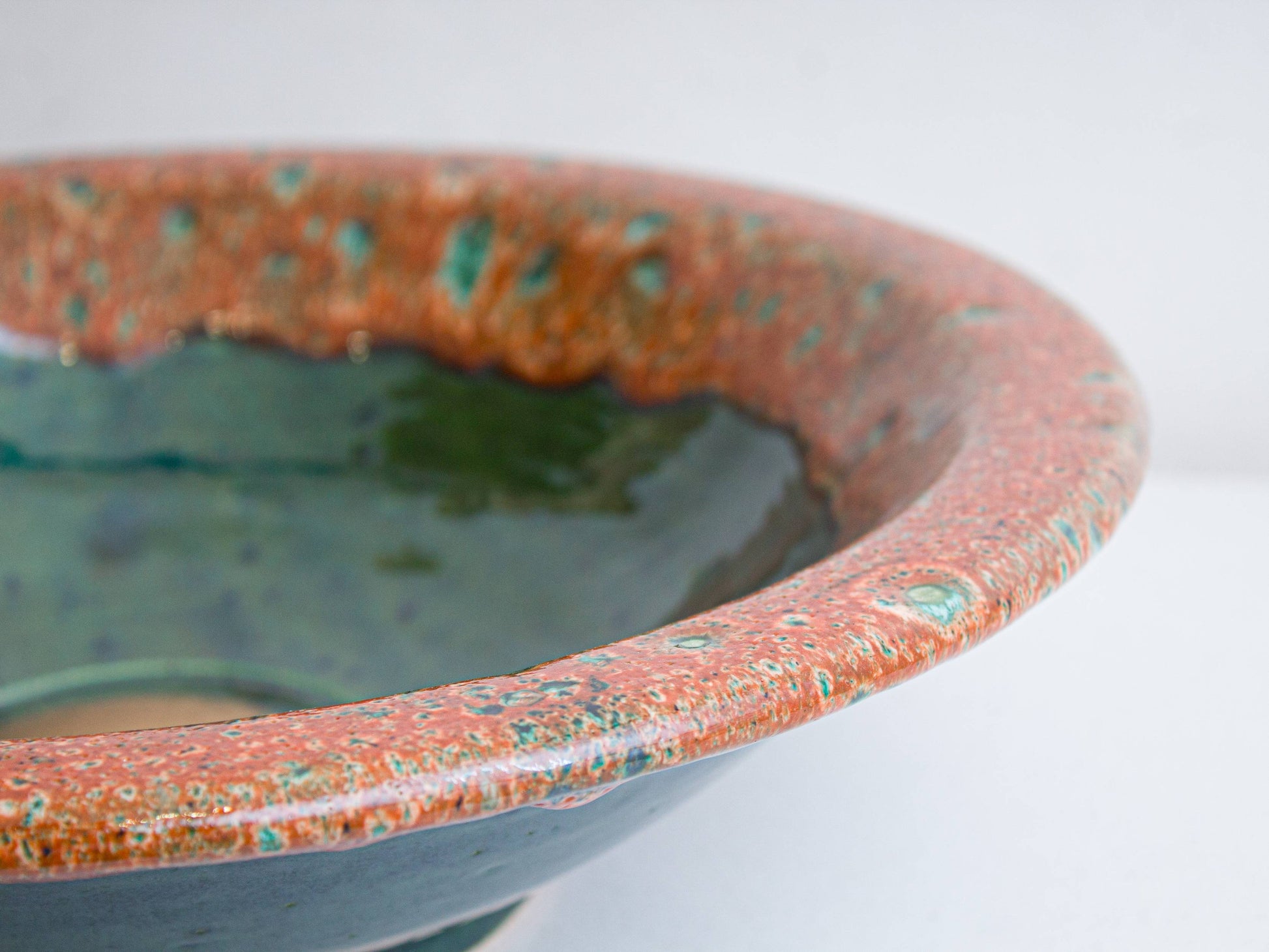 Close-up of hand-painted turquoise speckles on coral glazed rim of ceramic sink
